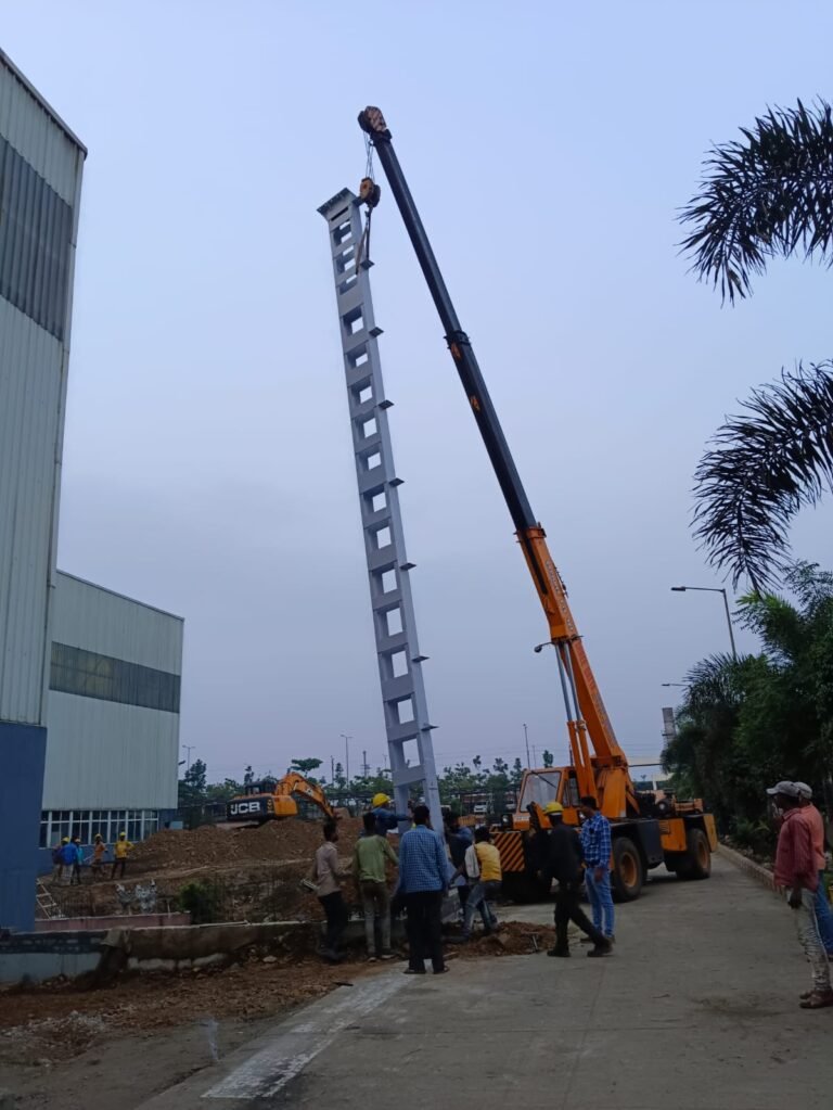 Crane lifting a tall lattice steel column while the team guides it