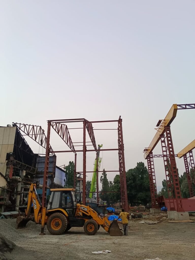 Red-primed steel frames standing on site with a backhoe loader